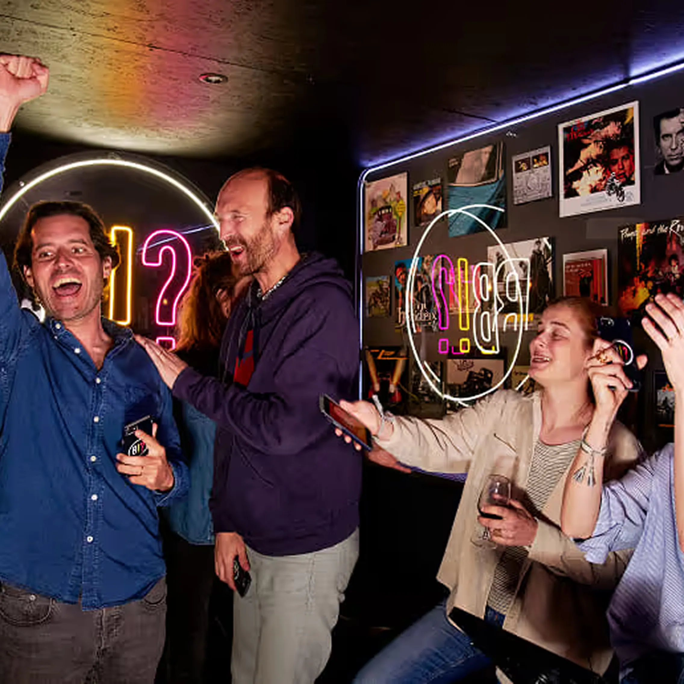Des joueurs debout dans un bar, smartphone en main, réagissant devant l’écran de jeu